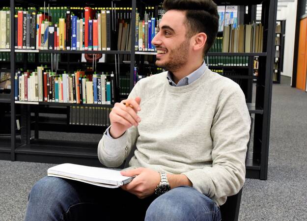 Scholarship recipient sitting in library smiling to something off camera