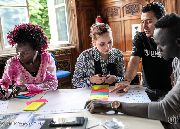 Ehab is sitting at a table brain storming with three other people during a UNHCR event. 