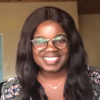 Young woman with long dark hair, glasses, and patterned top smiles at the camera 